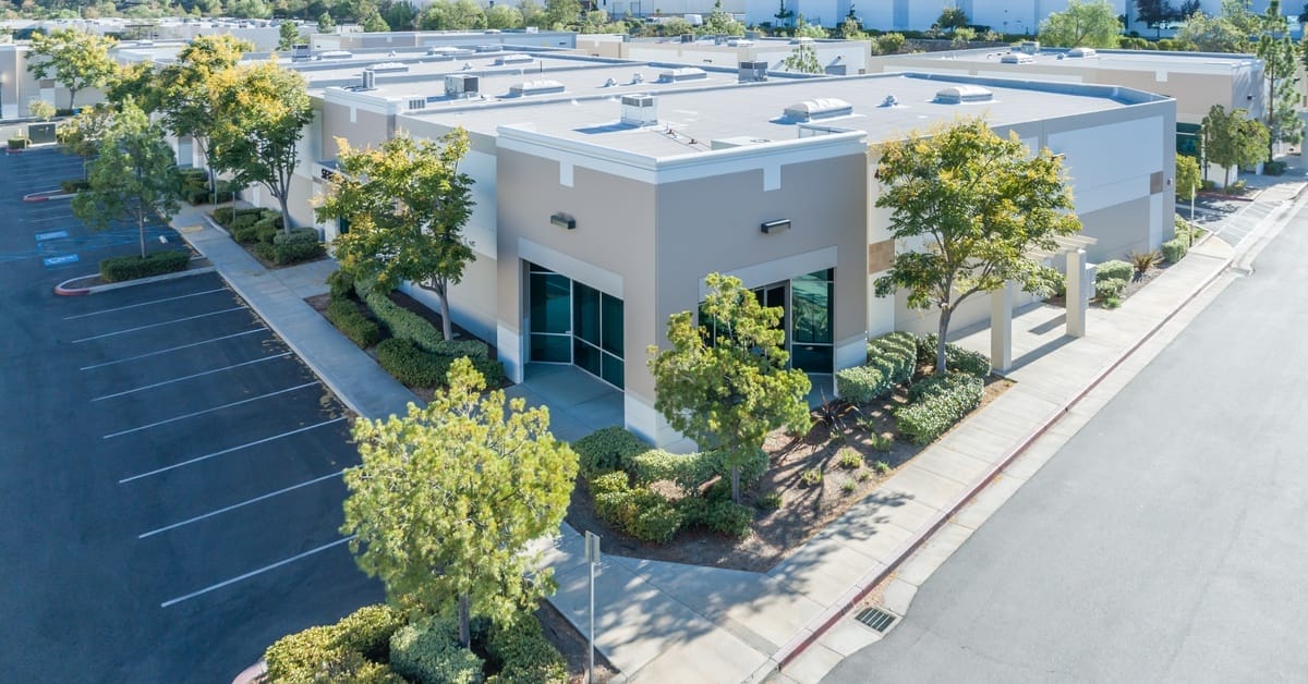 Aerial view of a large commercial office building and an empty parking lot on a sunny day. The space is landscaped.