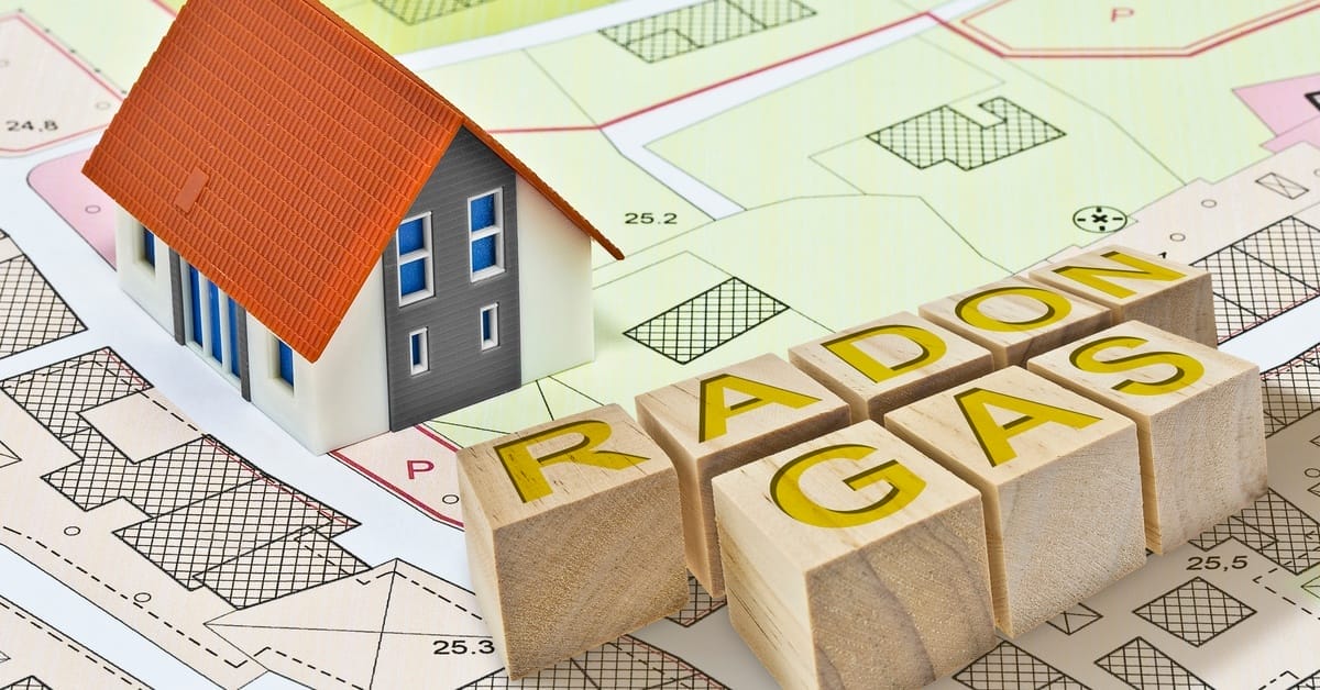 A mini house and wooden blocks spell "Radon Gas" sit on top of a blueprint of businesses and plot lines.